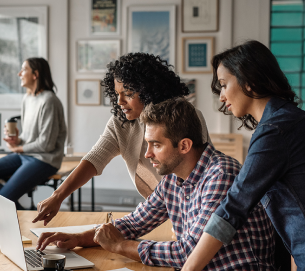 Three people at desk looking at computer.