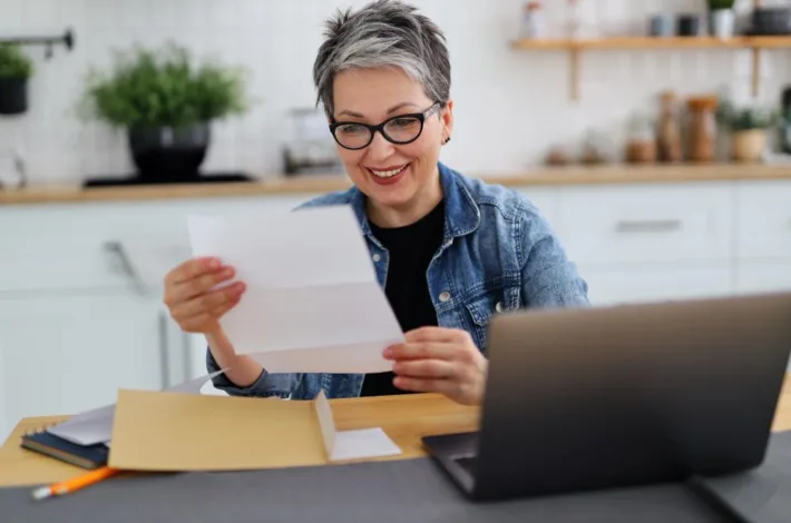 woman with short gray hair and glasses smiles looking at a piece of paper