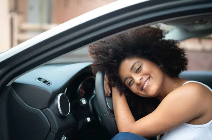 Black woman with natural hair smiles while holding the steering wheel in her car