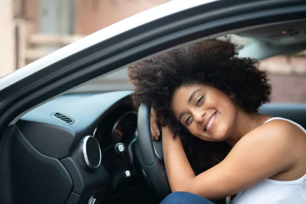 Black woman with natural hair smiles while holding the steering wheel in her car