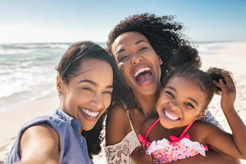 two women hold a small child taking selfie at the beach