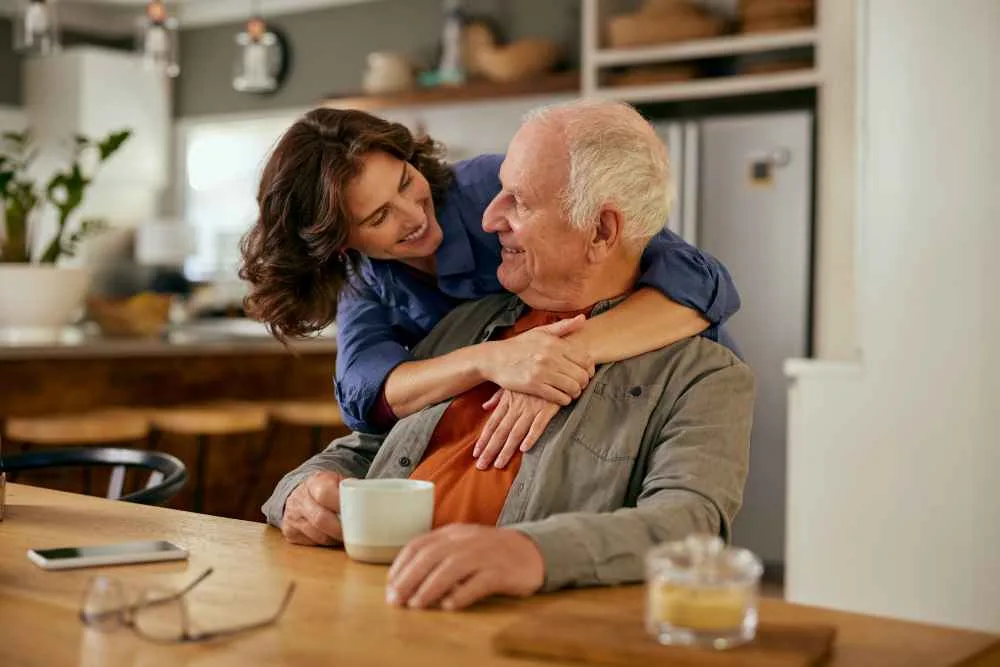 Women hugs elderly man at kitchen table