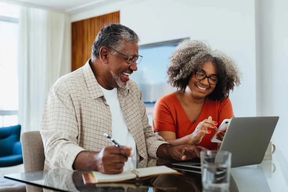 Smiling senior couple working on budget at home with a laptop and smartphone, discussing finances.