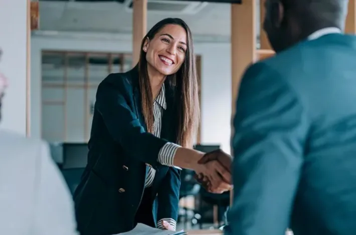 Woman smiling and shaking hands across a desk