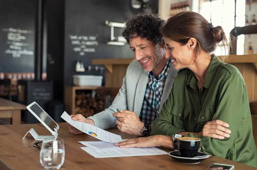 Man and woman business partners look over charts while drinking coffee
