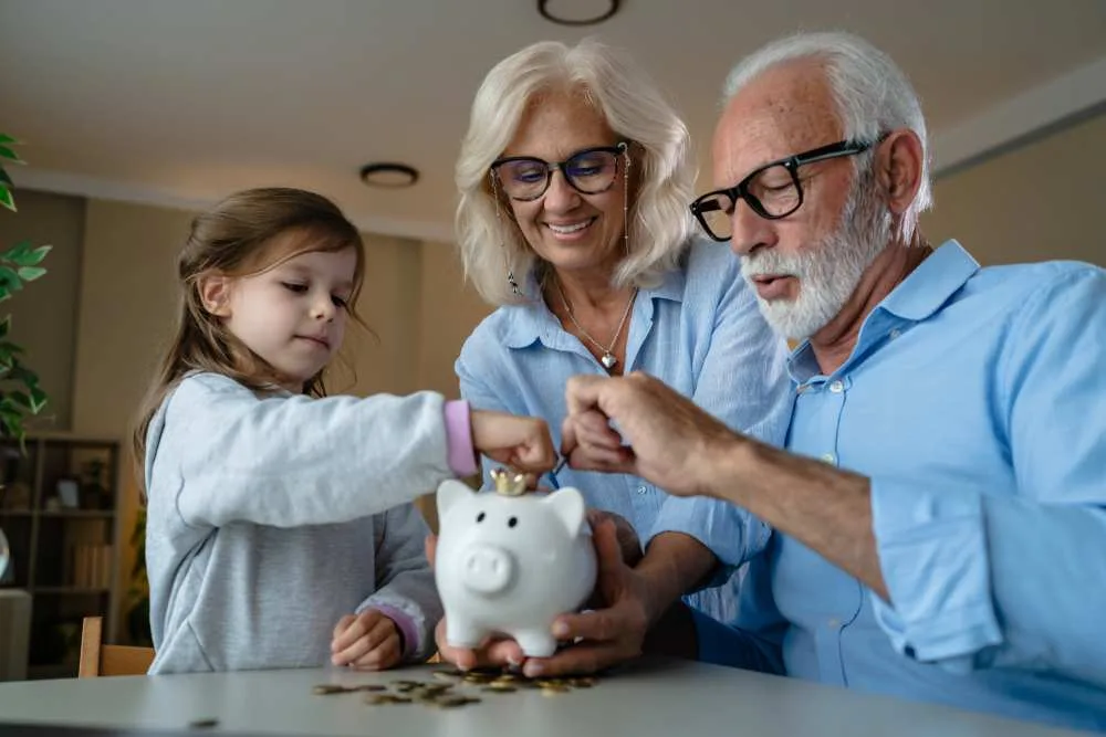 Grandparents and granddaughter put coins into a piggybank