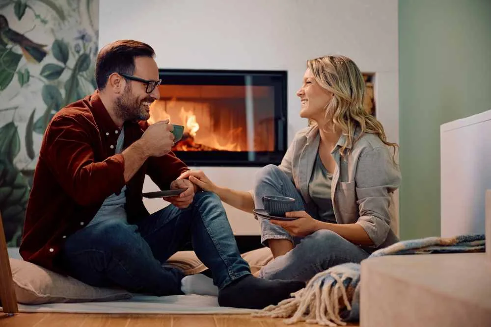 Male and female couple sit in front of fire place drinking coffee