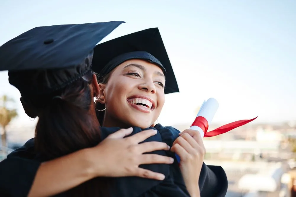 Woman graduating college holds diploma, hugs friend