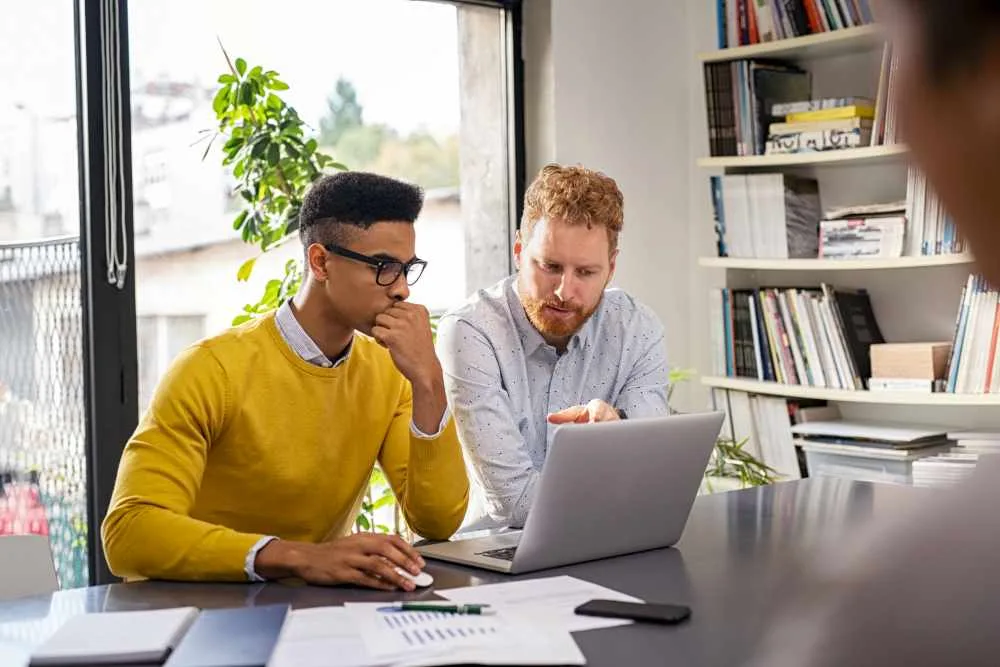Two men work at laptop in office setting