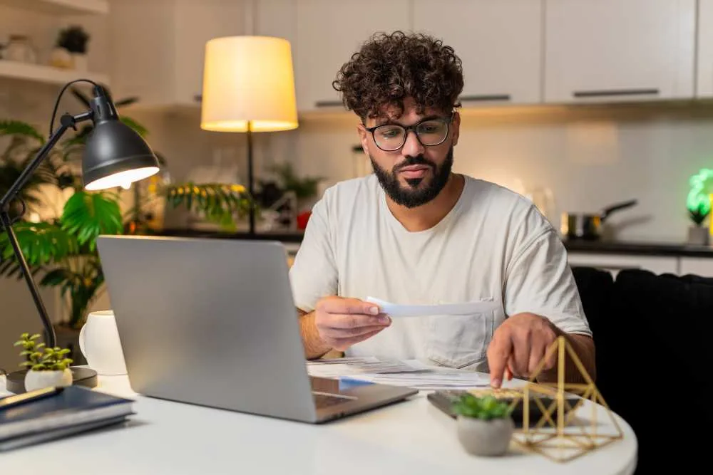 Young man works on taxes on laptop at table