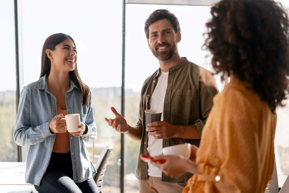 Three young professionals are taking a break from work, drinking coffee and chatting together in a modern office