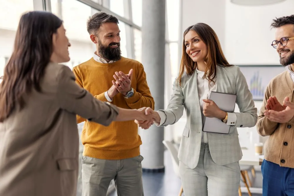 Two women shake hands while two men applaud